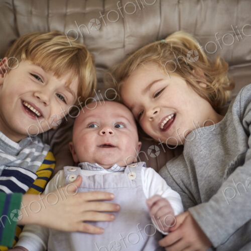 Three children lying on a bed, a boy and girl with a baby between them. Three children lying on a bed, a boy and girl with a baby between them.