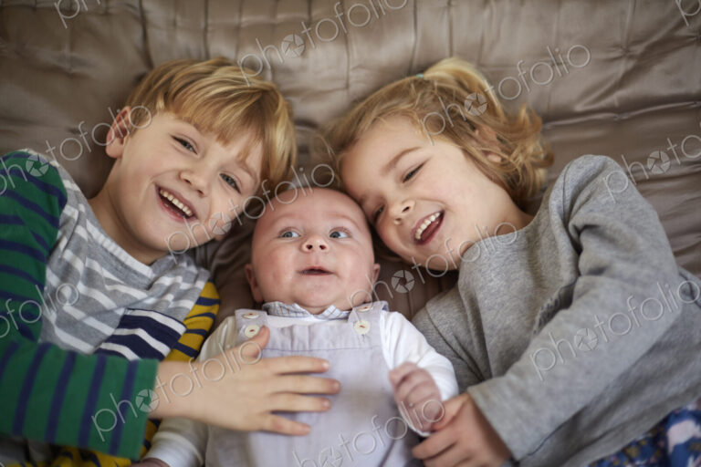 Three children lying on a bed, a boy and girl with a baby between them.