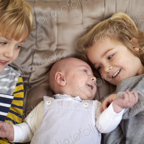 Three children lying on a bed, a boy and girl with a baby between them. Three children lying on a bed, a boy and girl with a baby between them.