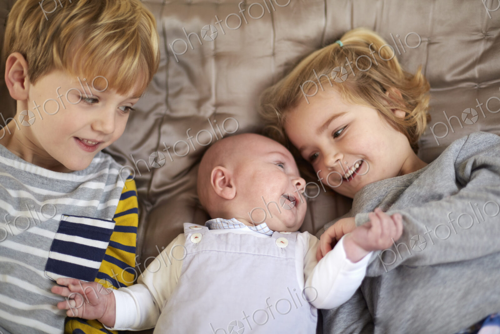 Three children lying on a bed, a boy and girl with a baby between them.