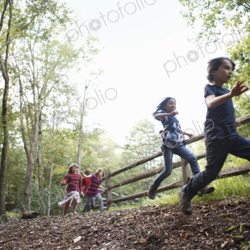 Three children playing around the farm, running around a paddock with wooden fencing. Three children playing around the farm, running around a paddock with wooden fencing.