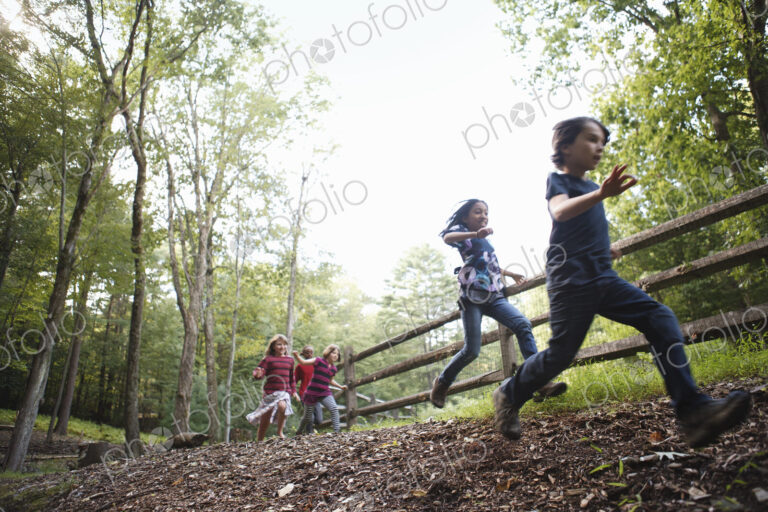 Three children playing around the farm, running around a paddock with wooden fencing.