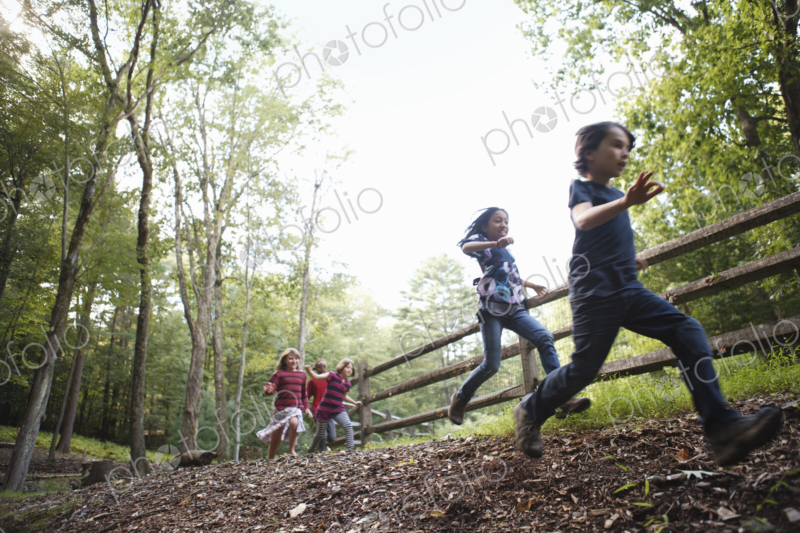 Three children playing around the farm, running around a paddock with wooden fencing.