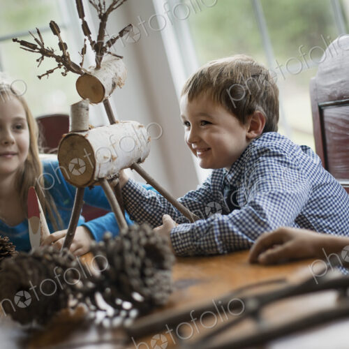 Three children sitting at a table in family home. A twig reindeer in the centre, with…