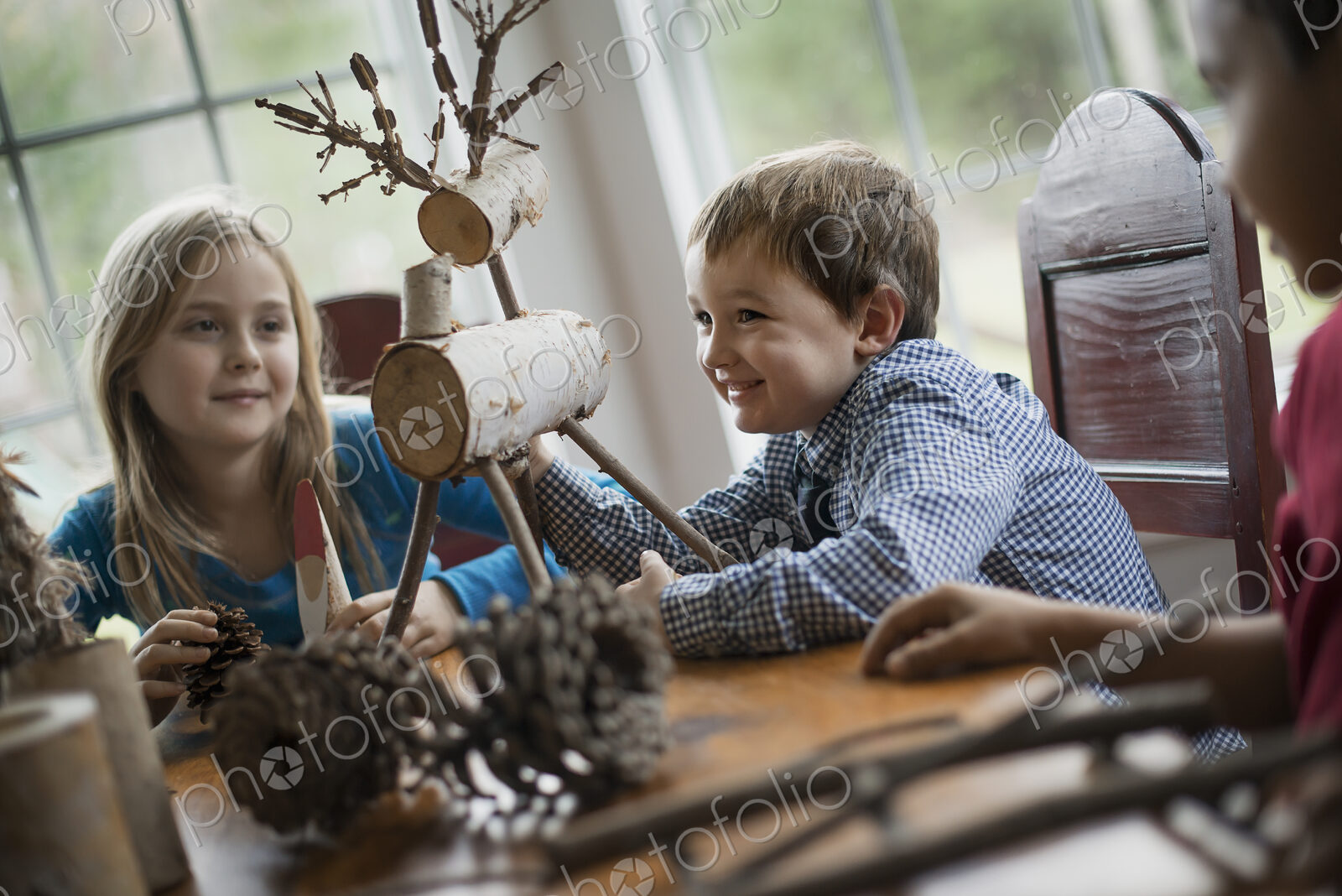 Three children sitting at a table in family home. A twig reindeer in the centre, with…