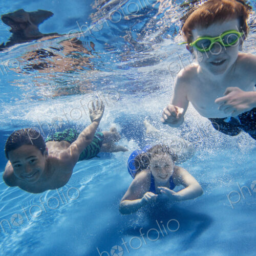 Three children swimming underwater, smiling at the camera. Three children swimming underwater, smiling at the camera.