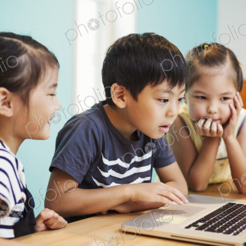 Three children using a laptop, two girls and a boy.