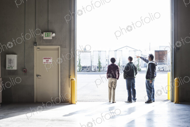 Three employees waiting for a product delivery in a loading dock door at a warehouse.