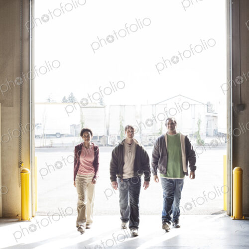 Three employees walking through the loading dock door of a distribution warehouse.