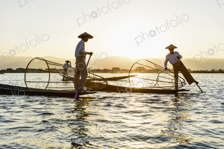 Three fisherman on Inle Lake, standing and using traditional rowing techniques,…