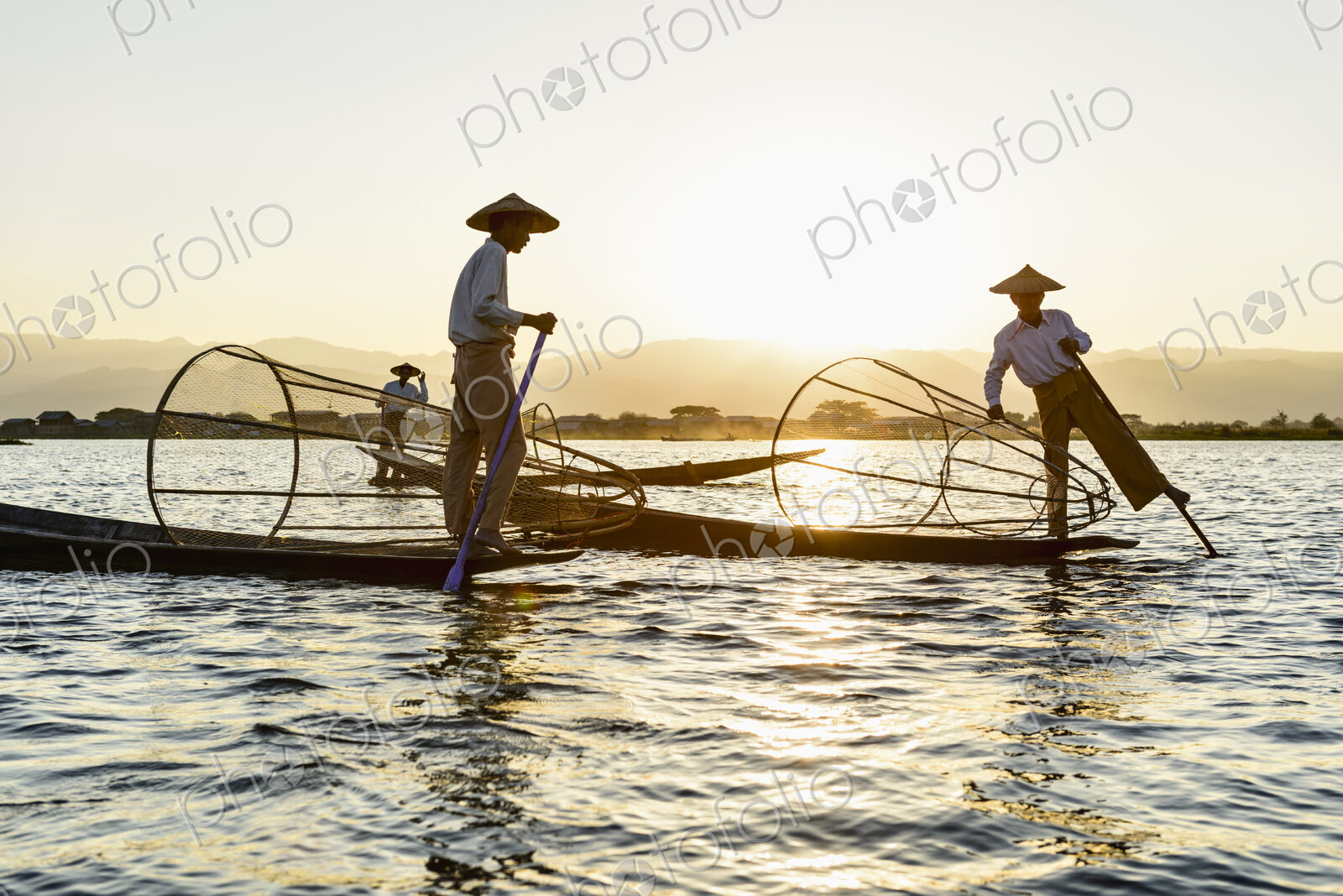 Three fisherman on Inle Lake, standing and using traditional rowing techniques,…