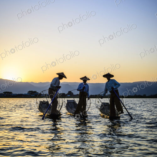 Three fishermen on Lake Inles, standing in their traditional boats.