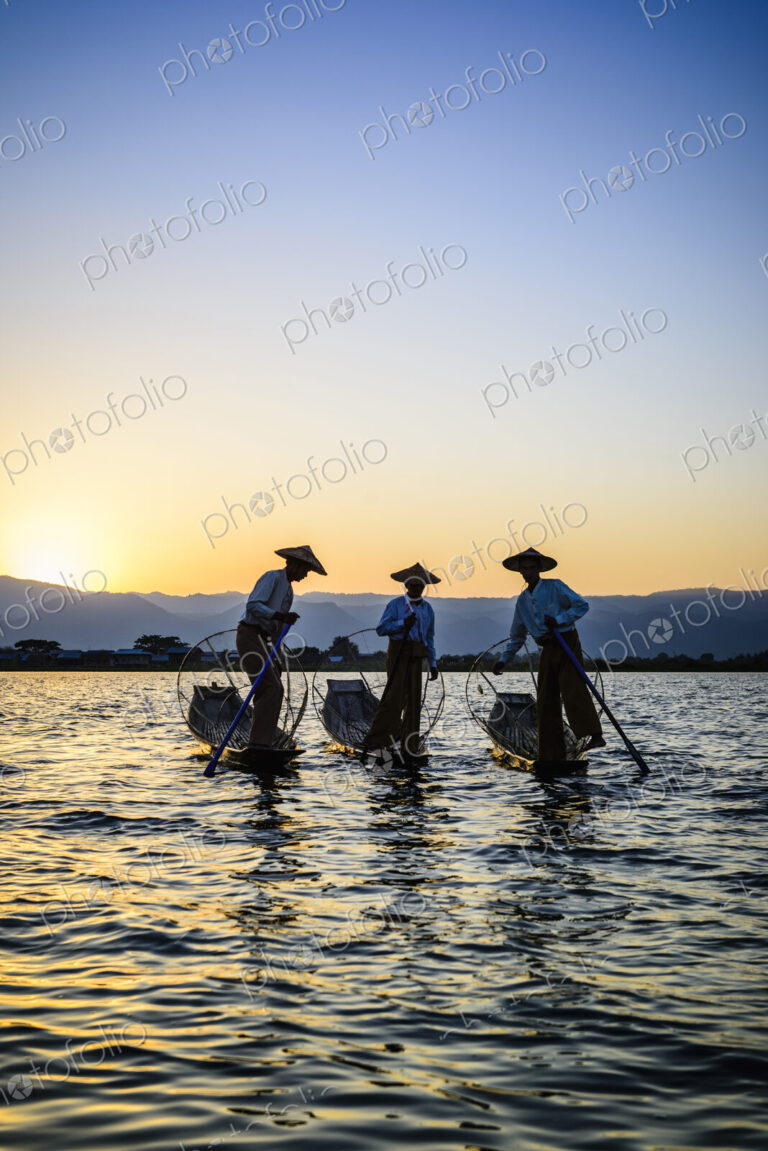 Three fishermen on Lake Inles, standing in their traditional boats.