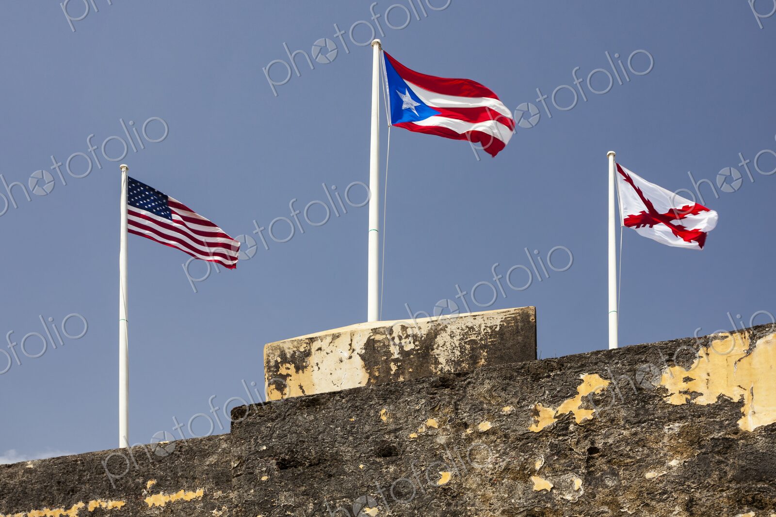 Three flags – the United States flag, the Puerto Rican flag, and the historic Cross of…