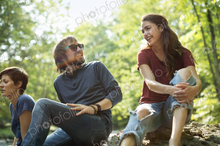Three friends by the riverbank laughing.