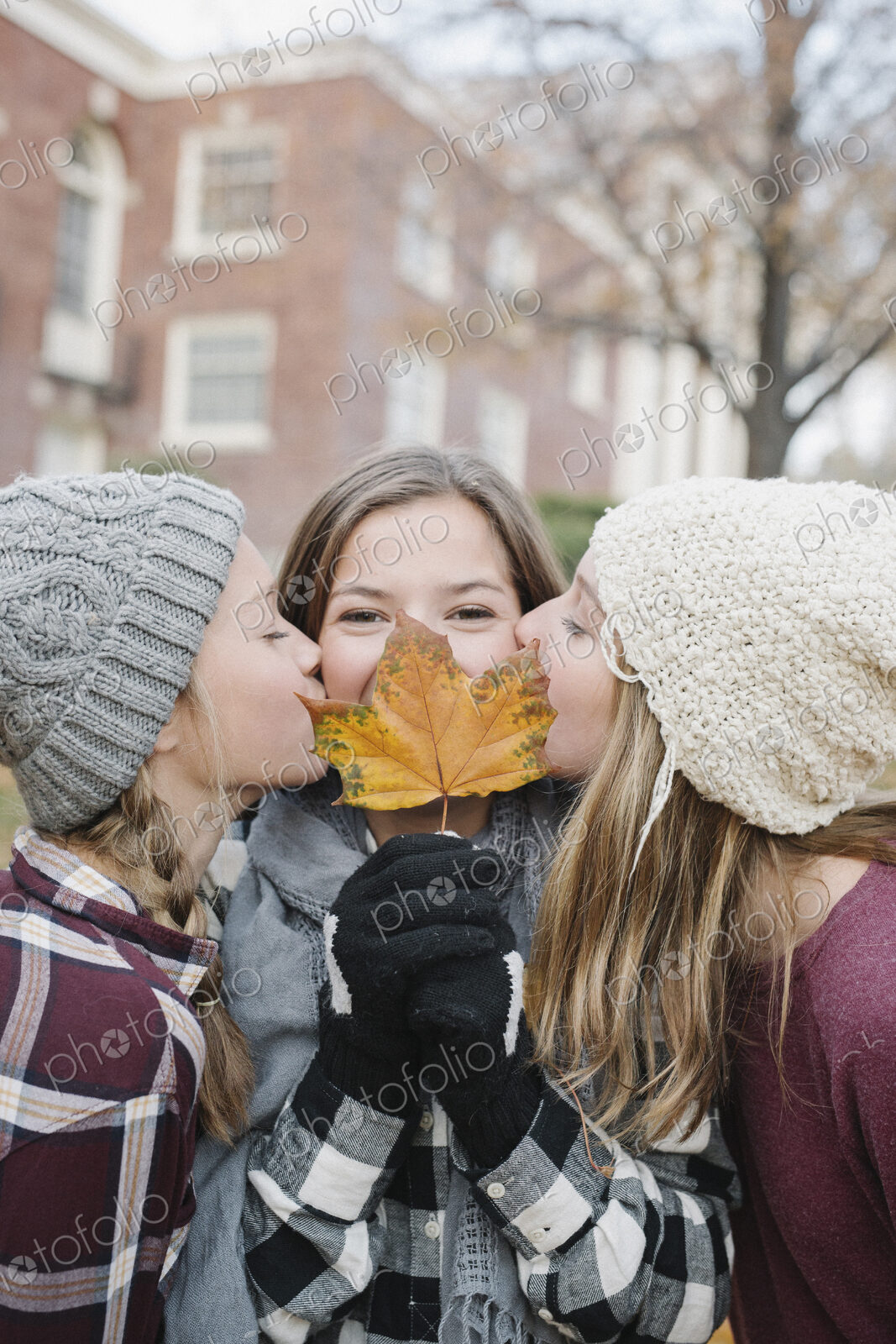 Three girls, one holding an autumn leaf by her face, two kissing her cheek.