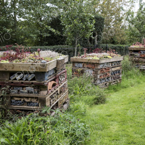 Three large bug houses with several layers of different materials in a garden.