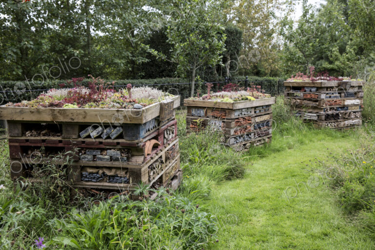 Three large bug houses with several layers of different materials in a garden.