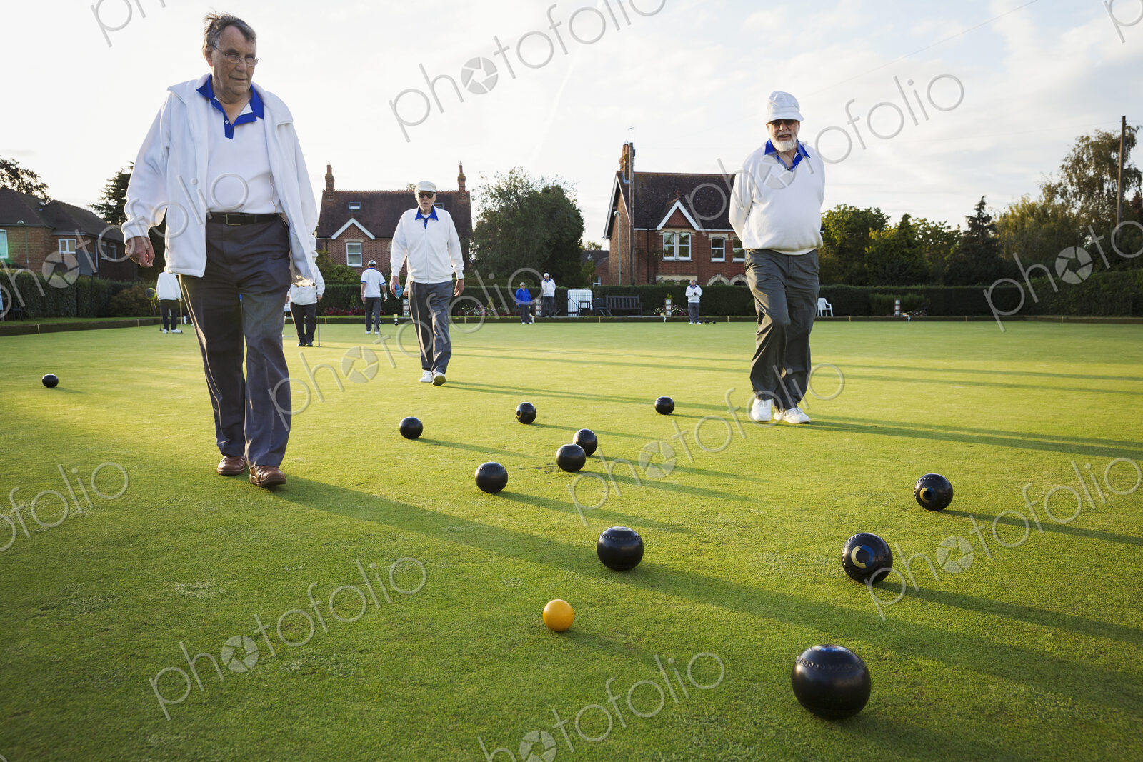 Three lawn bowls players, men walking across the green, the playing surface, at an end…