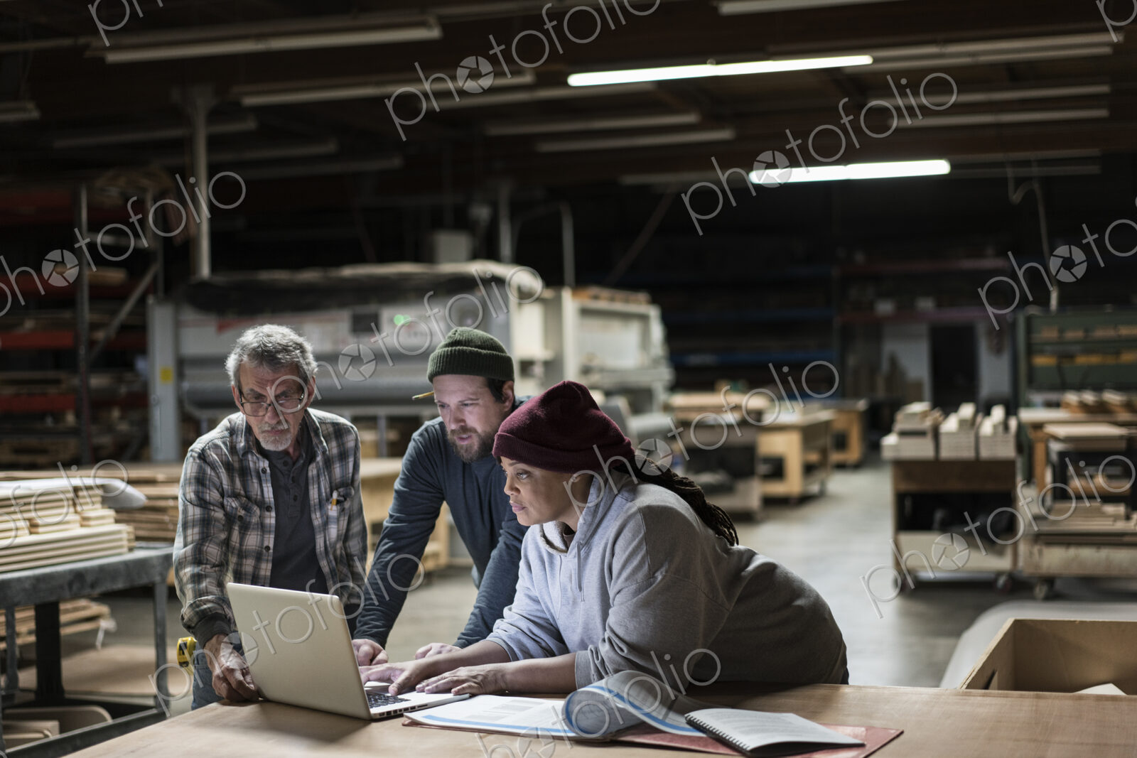 Three mixed race carpenters workng on a laptop computer after work hours in a large…