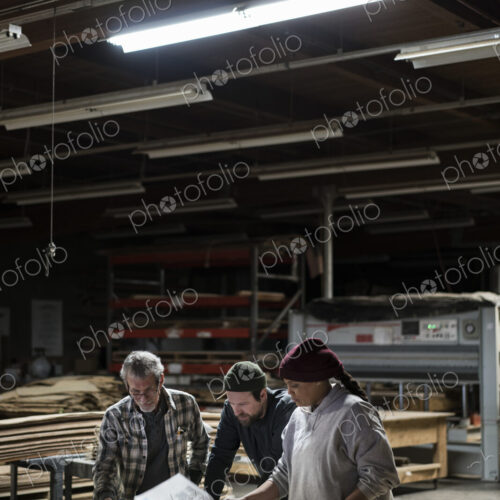 Three mixed race carpenters workng on a laptop computer after work hours in a large… Three mixed race carpenters workng on a laptop computer after work hours in a large…
