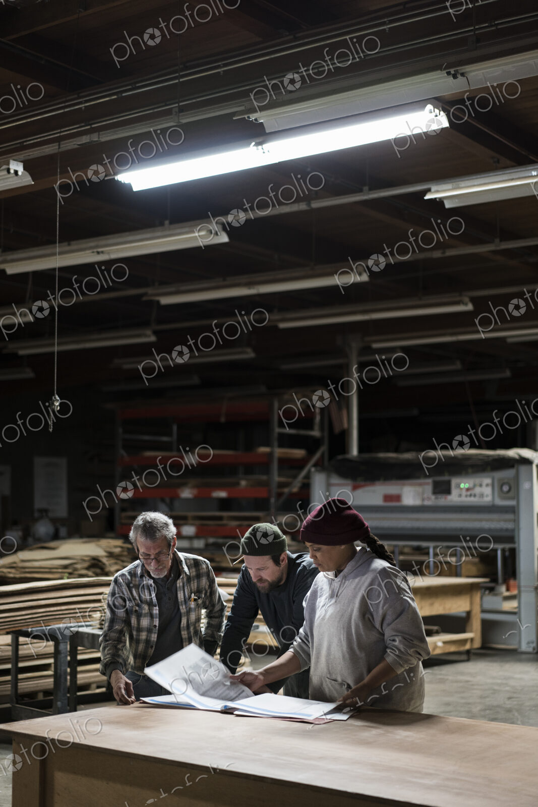 Three mixed race carpenters workng on a laptop computer after work hours in a large…