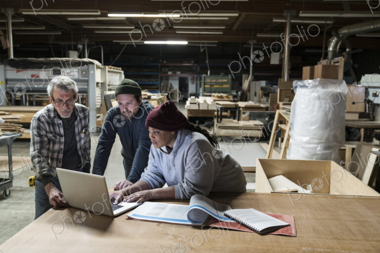 Three mixed race carpenters workng on a laptop computer after work hours in a large…