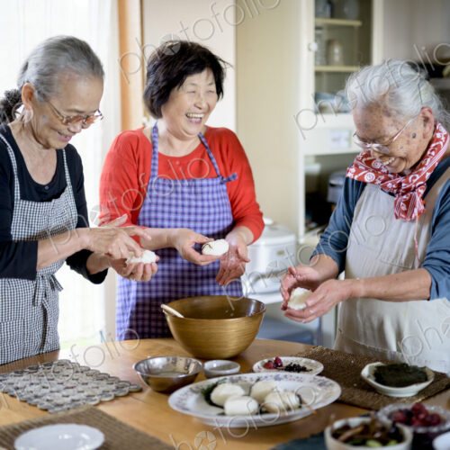 Three older women standing round a table in a kitchen, making sushi.