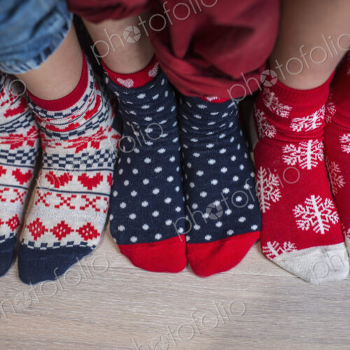 Three pairs of children's feet in bright patterned Christmas socks.