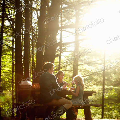 Three people, a family sitting at a picnic table under trees, in the late afternoon. Three people, a family sitting at a picnic table under trees, in the late afternoon.