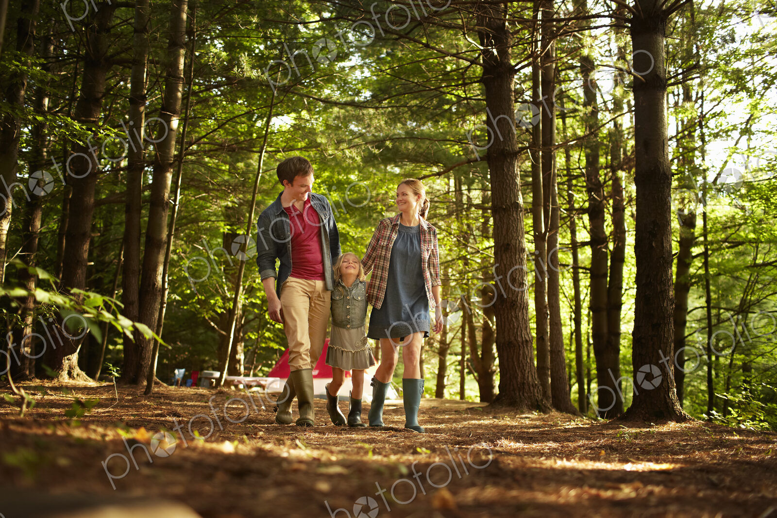 Three people, a family walking in woodland in the late afternoon.