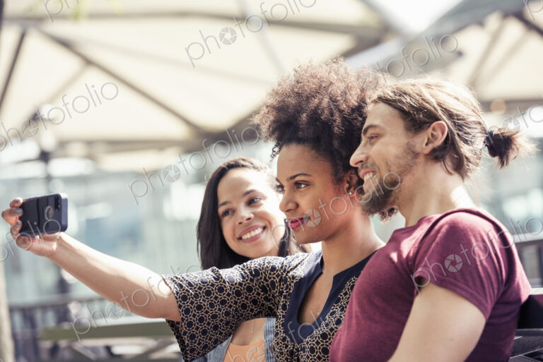 Three people, a man and two women, taking selfies in a city park