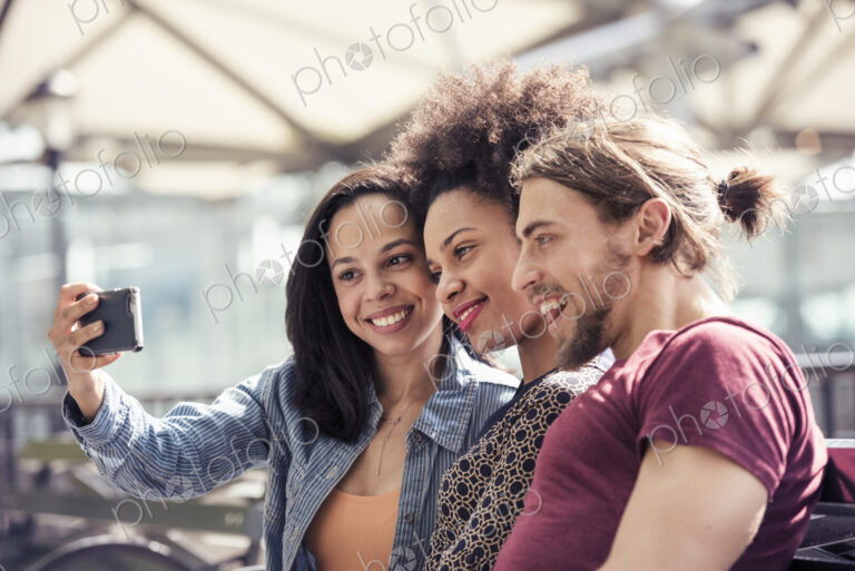 Three people, a man and two women, taking selfies in a city park