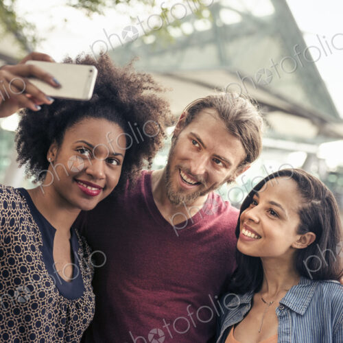 Three people, a man and two women, taking selfies in the park