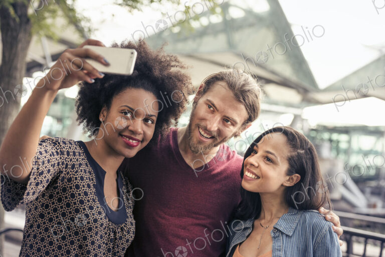 Three people, a man and two women, taking selfies in the park