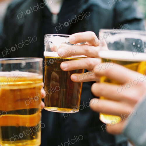 Three people drinking pints of beer, clinking glasses and toasting each other.