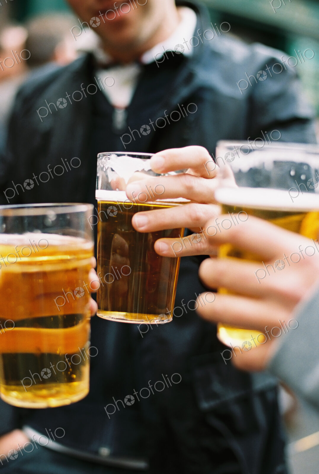 Three people drinking pints of beer, clinking glasses and toasting each other.
