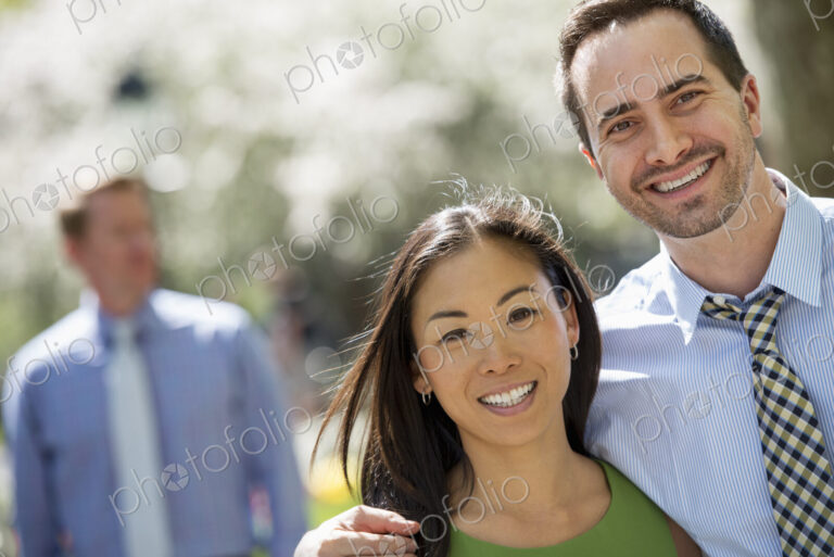 Three people in business dress. A couple side by side smiling at the camera. A man in…