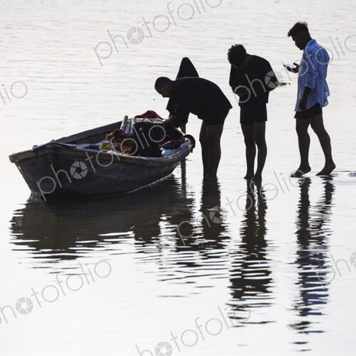 Three people in shallow water, one holding a small wooden boat, silhouettes. Three people in shallow water, one holding a small wooden boat, silhouettes.