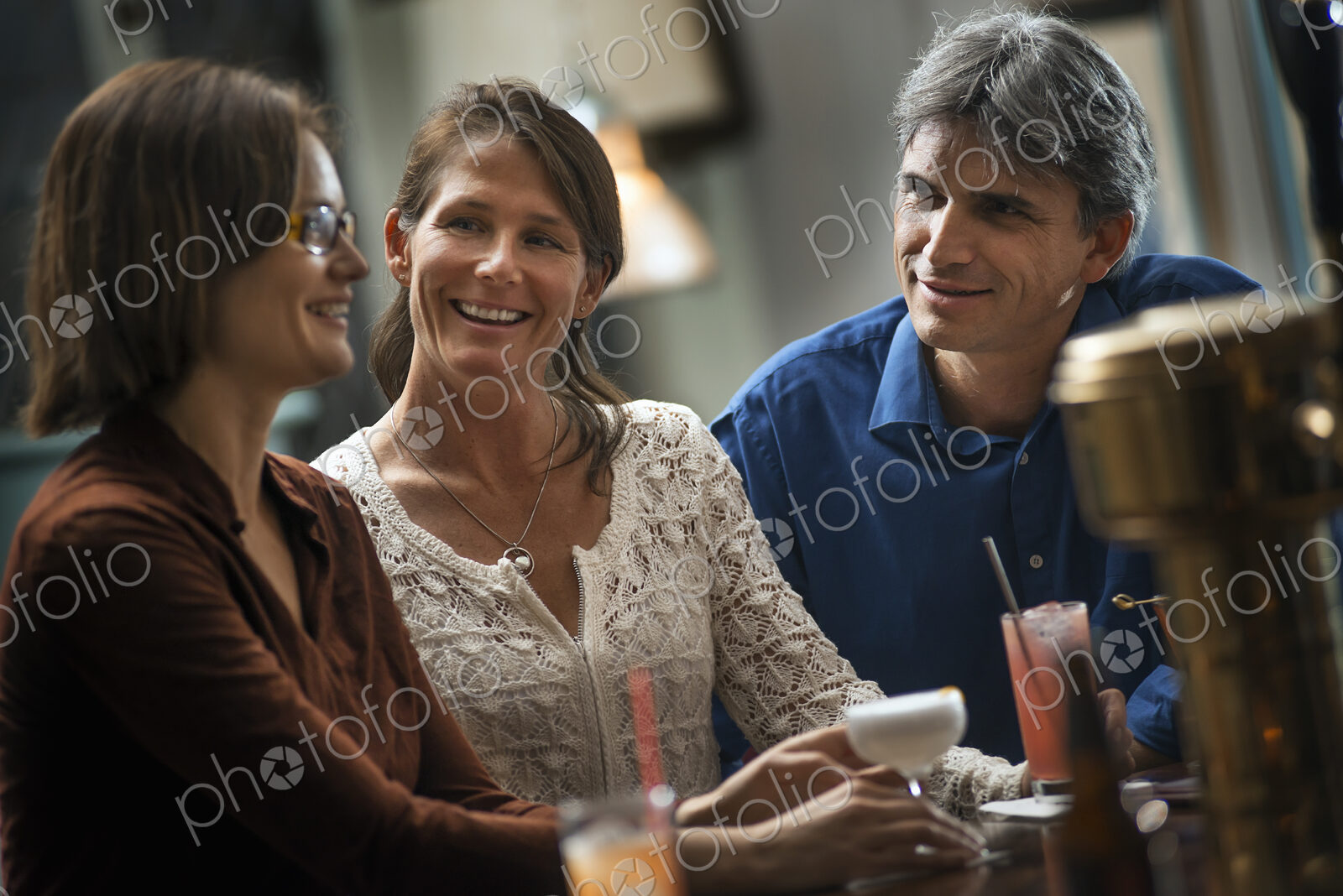 Three people meeting for a drink. Two women and a man sitting at a bar. Friends…
