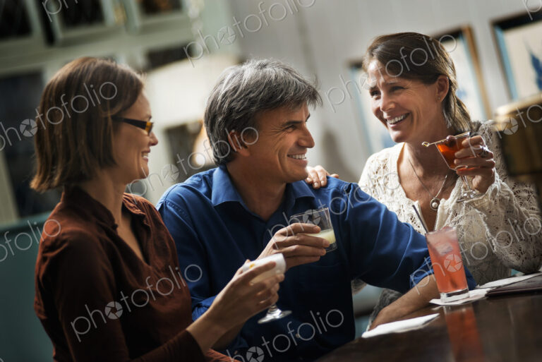 Three people meeting for a drink. Two women and a man sitting at a bar. Friends…