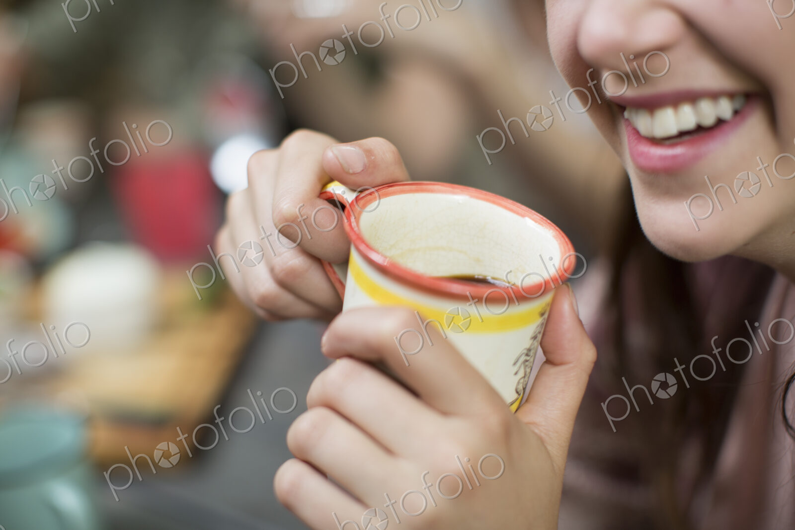 Three people seated around a table in a woodland clearing, one holding a mug with both…
