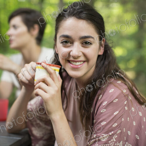 Three people seated around a table in a woodland clearing, one woman smiling at the… Three people seated around a table in a woodland clearing, one woman smiling at the…