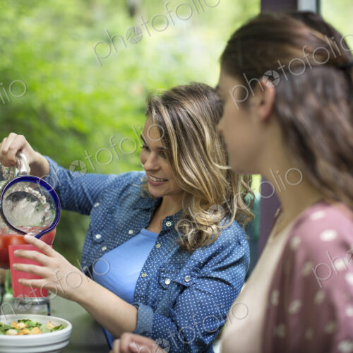 Three people seated at a table in woodland, having a meal, one woman pouring juice… Three people seated at a table in woodland, having a meal, one woman pouring juice…