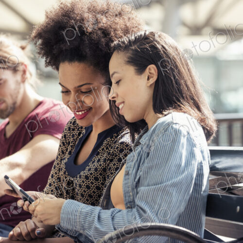 Three people seated side by side on a park bench checking their smart phones Three people seated side by side on a park bench checking their smart phones