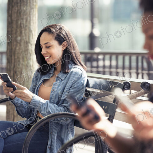 Three people seated side by side on a park bench checking their smart phones Three people seated side by side on a park bench checking their smart phones