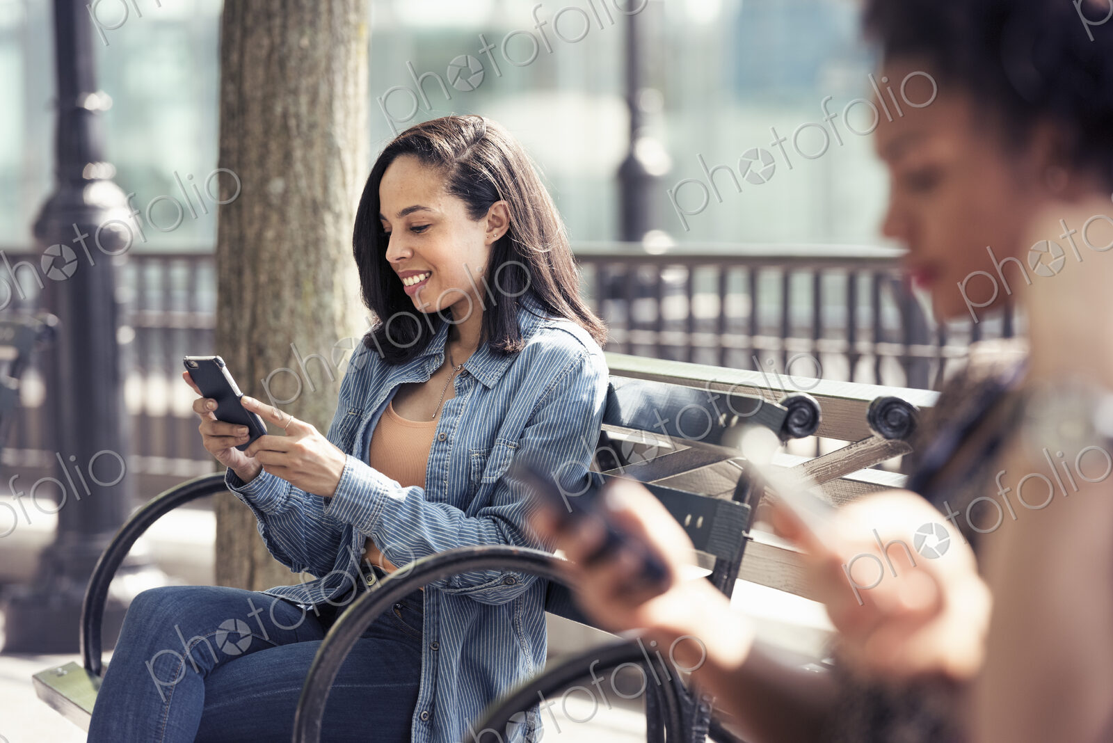 Three people seated side by side on a park bench checking their smart phones
