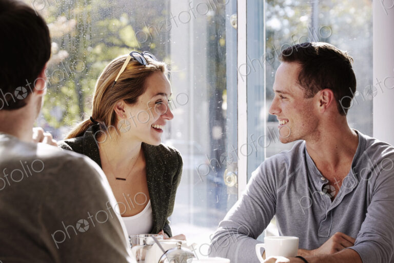 Three people sitting at a table talking, with mugs and jars of smoothies.