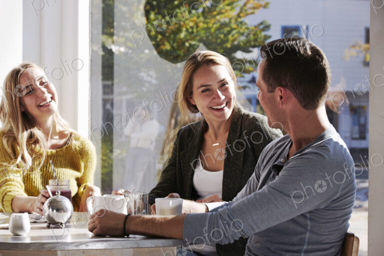 Three people sitting at a table talking, with mugs and jars of smoothies.