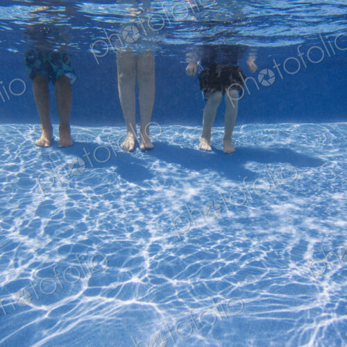 Three people standing on the bottom of a swimming pool. View from the knees down. Three people standing on the bottom of a swimming pool. View from the knees down.